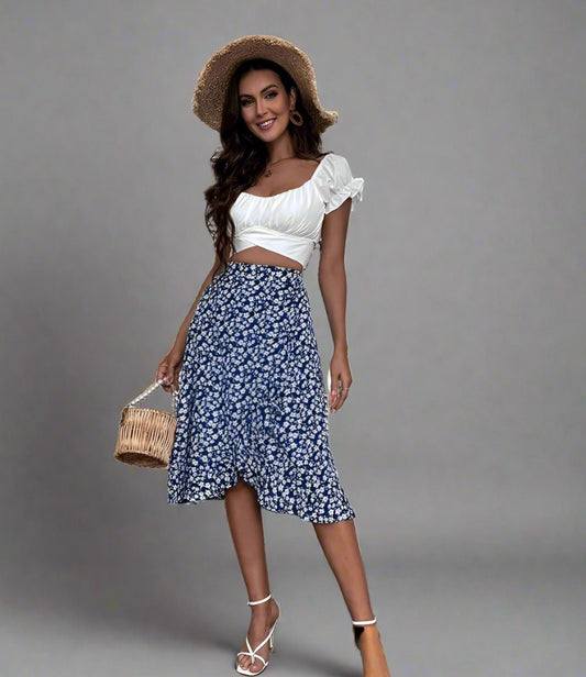 Woman wearing a blue midi skirt with a white floral print, paired with a white crop top and white strappy heels